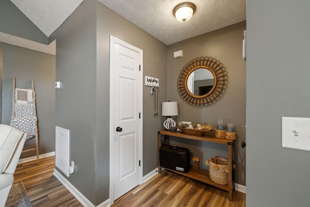 hall with a textured ceiling, visible vents, and wood finished floors