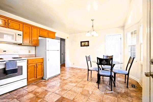 kitchen featuring white appliances, brown cabinetry, pendant lighting, a chandelier, and baseboards