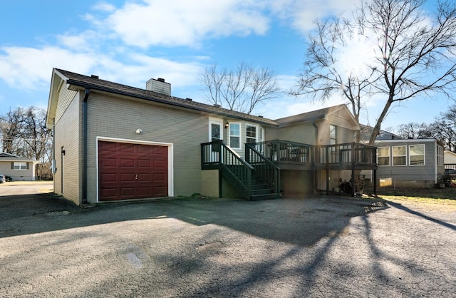 back of house featuring a chimney, brick siding, a wooden deck, and asphalt driveway
