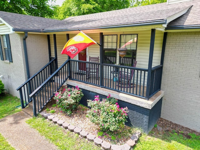 view of exterior entry featuring roof with shingles, brick siding, and covered porch