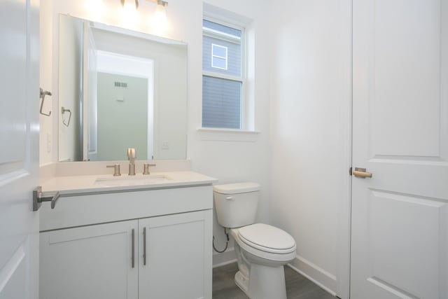 bathroom featuring wood finished floors, toilet, vanity, baseboards, and visible vents