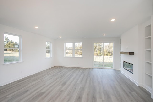 unfurnished living room featuring a glass covered fireplace, light wood-type flooring, recessed lighting, and built in shelves