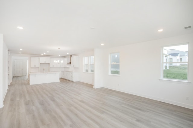 unfurnished living room with a notable chandelier, light wood-style floors, and baseboards