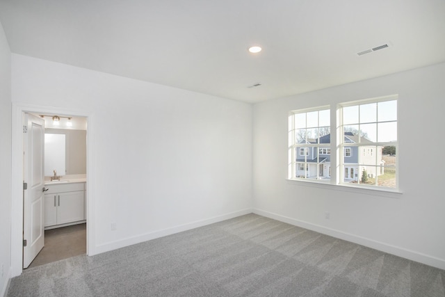 empty room featuring baseboards, visible vents, light colored carpet, and a sink
