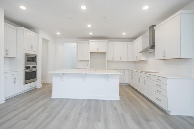 kitchen featuring a kitchen island with sink, decorative backsplash, stainless steel appliances, a sink, and wall chimney exhaust hood