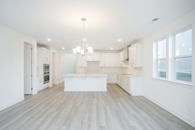 kitchen featuring a kitchen island with sink, an inviting chandelier, stainless steel appliances, light wood-style floors, and baseboards