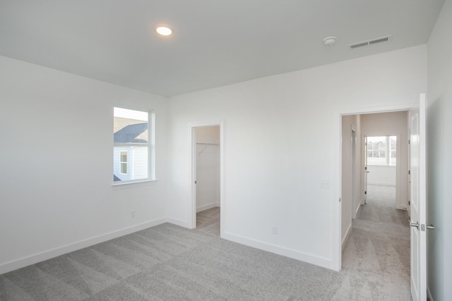 unfurnished bedroom with visible vents, multiple windows, light colored carpet, and baseboards