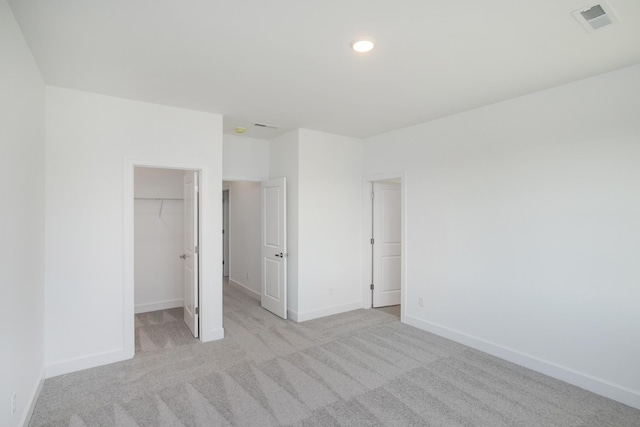 unfurnished bedroom featuring a spacious closet, a closet, light carpet, baseboards, and visible vents