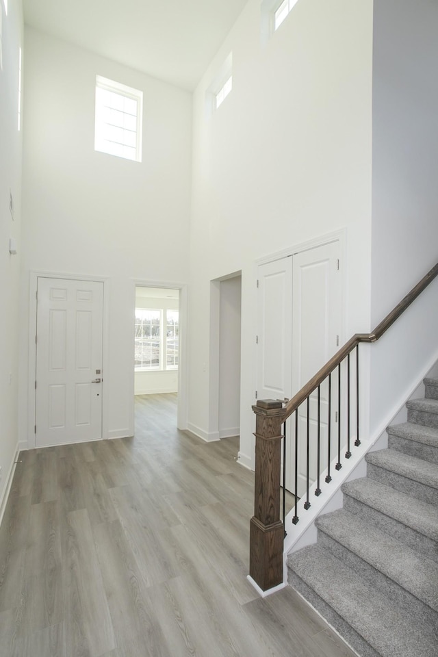 entrance foyer featuring baseboards, stairway, light wood-style floors, and a towering ceiling