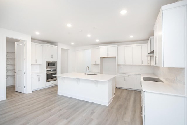 kitchen featuring a sink, appliances with stainless steel finishes, light wood-style floors, recessed lighting, and an island with sink