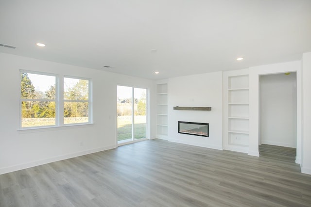unfurnished living room with visible vents, baseboards, a glass covered fireplace, wood finished floors, and built in shelves