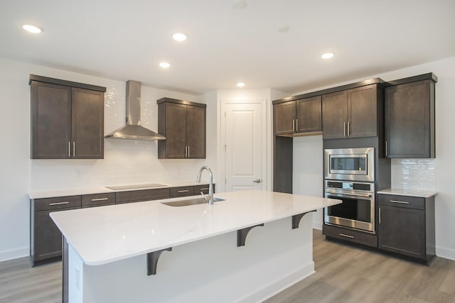 kitchen with light wood-style flooring, stainless steel appliances, wall chimney range hood, and a sink