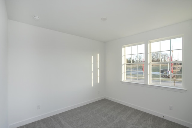 spare room with baseboards and dark carpet