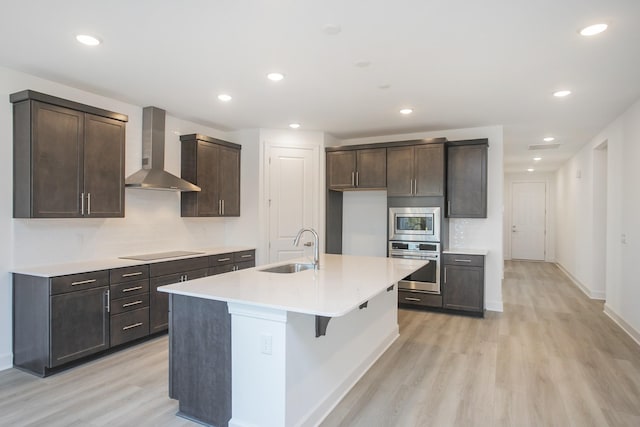 kitchen featuring appliances with stainless steel finishes, a sink, light wood-style floors, and wall chimney exhaust hood