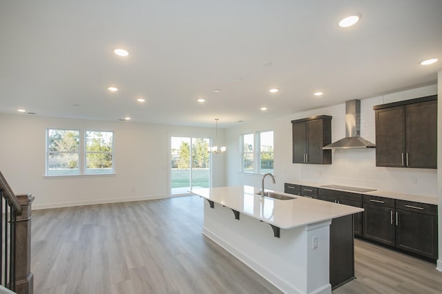 kitchen featuring an inviting chandelier, light wood-style flooring, light countertops, wall chimney range hood, and a sink