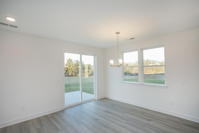unfurnished dining area featuring an inviting chandelier, wood finished floors, visible vents, and baseboards