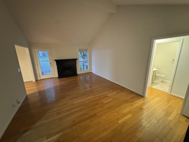 unfurnished living room with baseboards, lofted ceiling with beams, a fireplace, and wood-type flooring