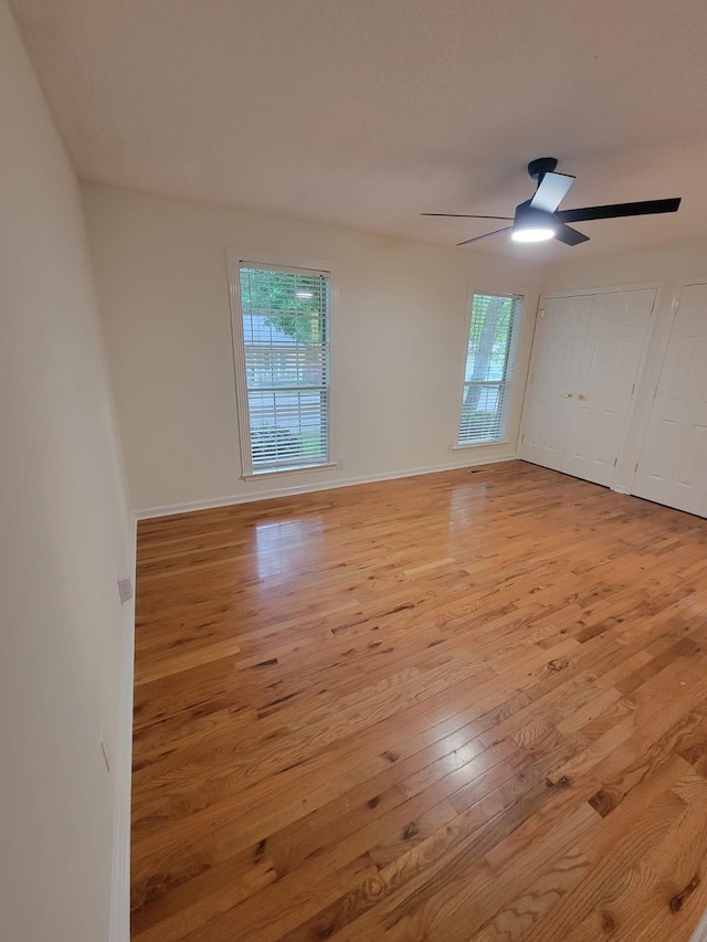 empty room with a ceiling fan, baseboards, a wealth of natural light, and light wood-style floors
