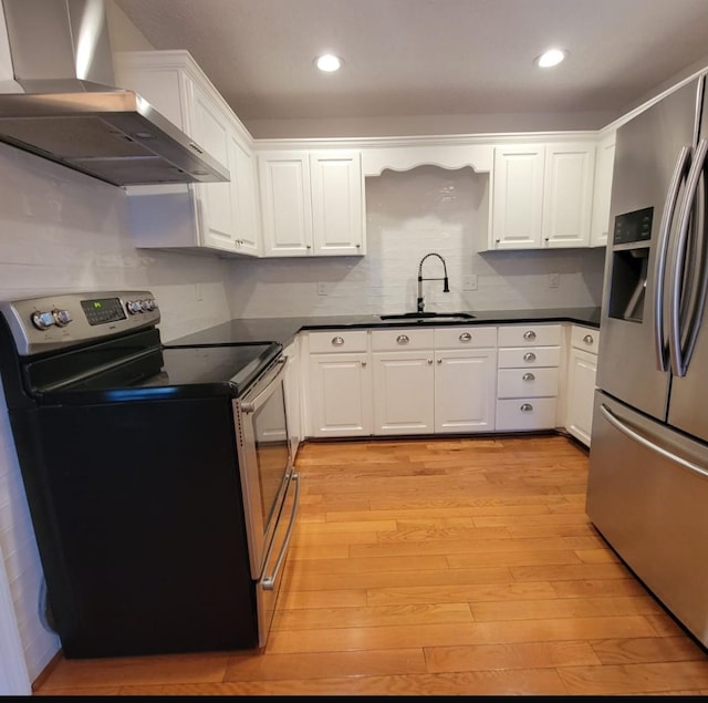 kitchen featuring a sink, appliances with stainless steel finishes, dark countertops, light wood-style floors, and wall chimney exhaust hood
