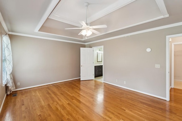 spare room featuring light wood-style flooring, ceiling fan, baseboards, crown molding, and a tray ceiling