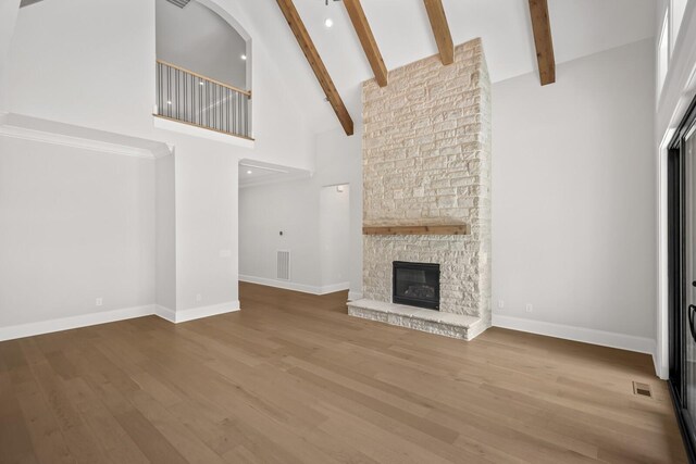 unfurnished living room featuring visible vents, beam ceiling, wood finished floors, high vaulted ceiling, and a stone fireplace