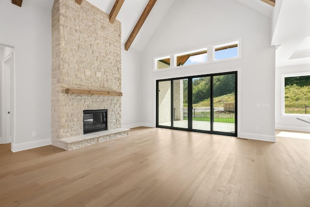 unfurnished living room with beamed ceiling, baseboards, wood finished floors, high vaulted ceiling, and a stone fireplace