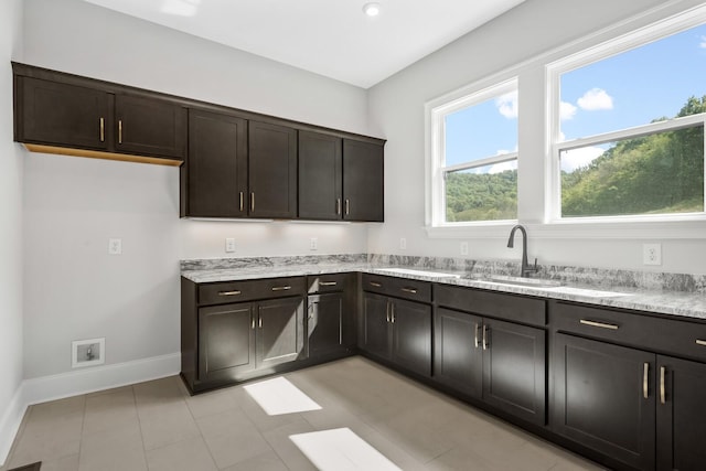 kitchen with dark brown cabinetry, light stone countertops, baseboards, and a sink