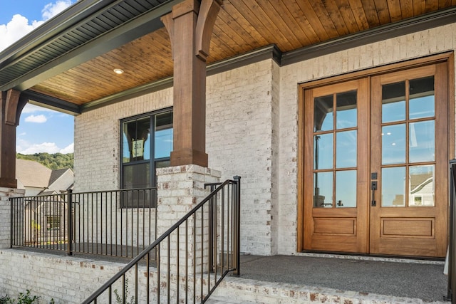 property entrance featuring covered porch, french doors, and brick siding