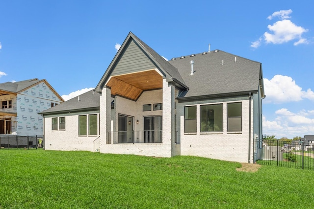 rear view of property featuring a lawn, fence, roof with shingles, and brick siding