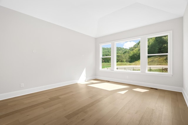 empty room with lofted ceiling, visible vents, wood finished floors, and baseboards