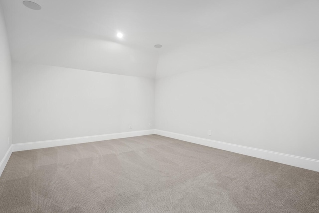 carpeted empty room featuring vaulted ceiling and baseboards