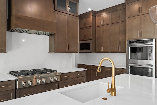 kitchen with stainless steel appliances, light countertops, premium range hood, and a sink