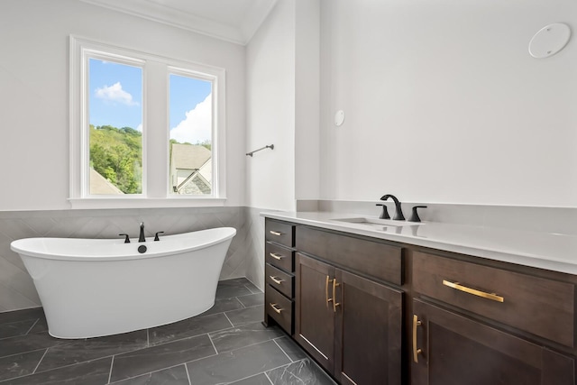 full bath featuring a freestanding bath, marble finish floor, tile walls, vanity, and crown molding