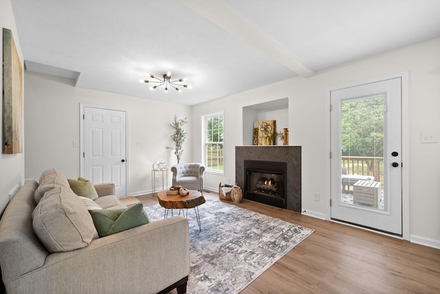 living room featuring beamed ceiling, a chandelier, a warm lit fireplace, baseboards, and wood finished floors