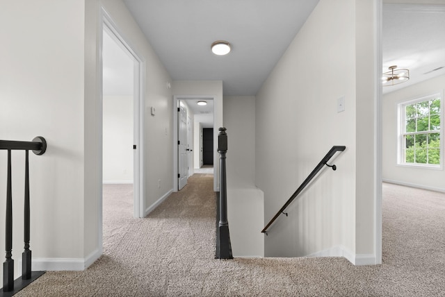 hallway with an upstairs landing, a chandelier, carpet, and baseboards