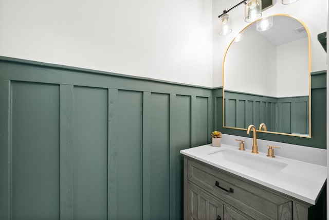 bathroom with vanity, visible vents, wainscoting, and a decorative wall