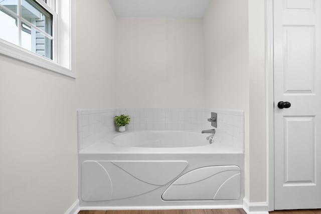 full bath with a bath, wood finished floors, and baseboards