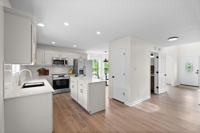 kitchen with tasteful backsplash, a sink, stainless steel appliances, light countertops, and light wood finished floors
