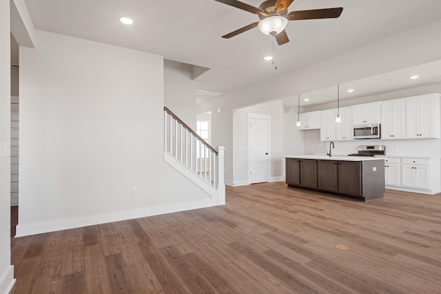 kitchen featuring a sink, stainless steel appliances, light wood-style floors, ceiling fan, and white cabinets
