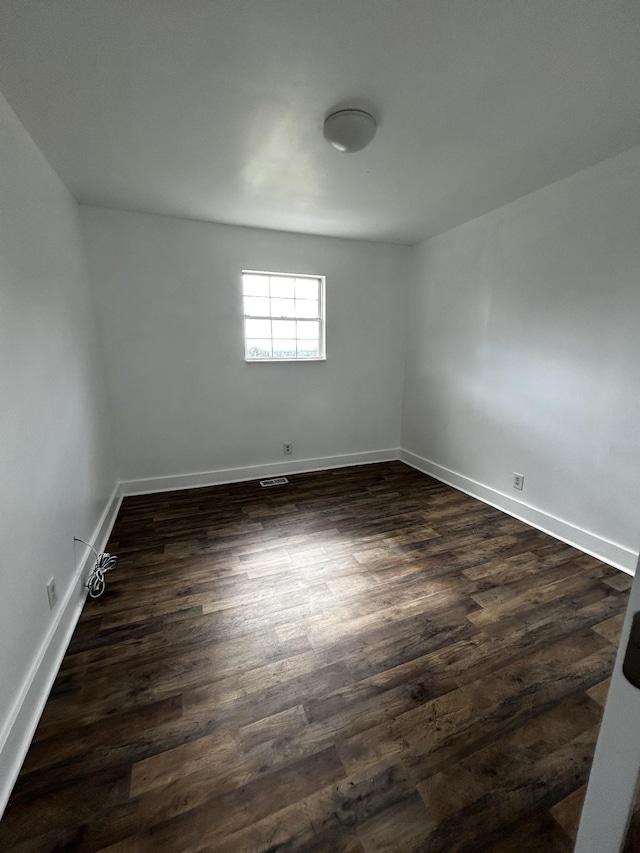 empty room featuring dark wood-type flooring, visible vents, and baseboards