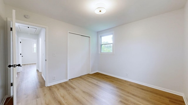 unfurnished bedroom featuring attic access, light wood-style flooring, and baseboards