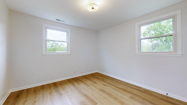 spare room with light wood finished floors, visible vents, and a healthy amount of sunlight