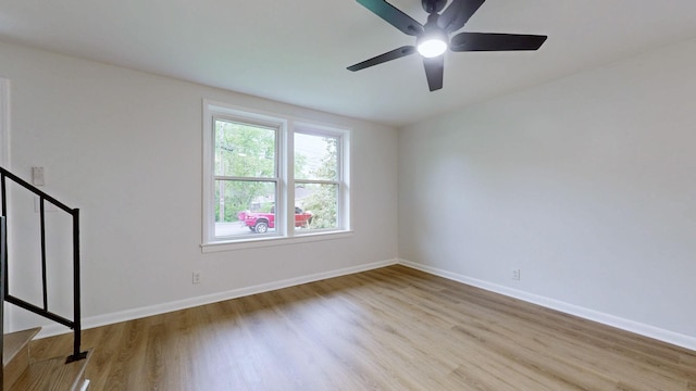 empty room with baseboards, stairway, wood finished floors, and ceiling fan