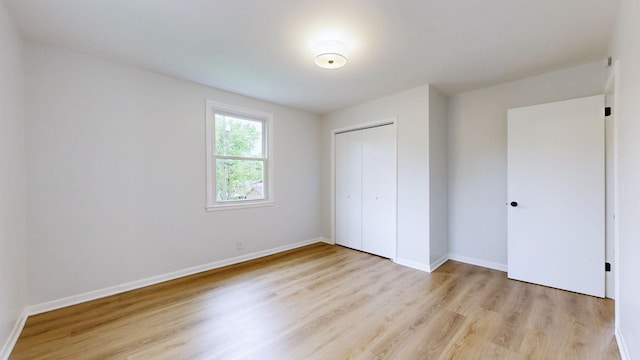 unfurnished bedroom featuring baseboards, light wood-type flooring, and a closet