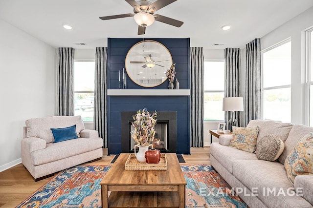 living room featuring ceiling fan, visible vents, a large fireplace, baseboards, and wood finished floors