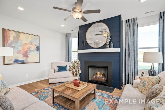 living room featuring wood finished floors, ceiling fan, a fireplace, baseboards, and visible vents