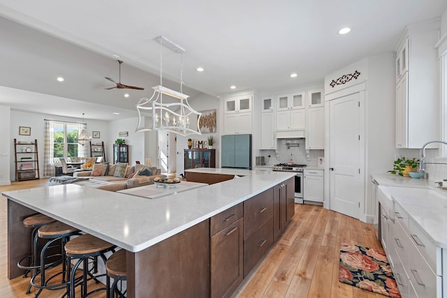 kitchen with gas stove, ceiling fan with notable chandelier, white cabinetry, a large island, and backsplash
