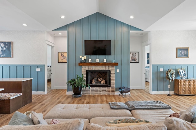 living area with a fireplace, wood finished floors, lofted ceiling, a decorative wall, and recessed lighting