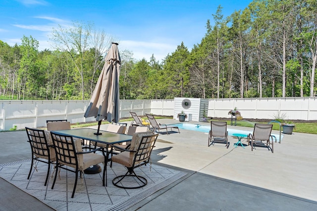 view of patio / terrace featuring a fenced in pool, a fenced backyard, outdoor dining area, and a forest view