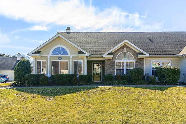 view of front of home featuring roof with shingles, a front yard, and stone siding
